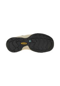 Black rubber outsole with multi-directional tread pattern, beige midsole, and blue accent near the heel. Brand logo visible on the sole.