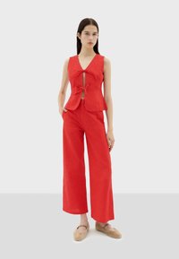 Red sleeveless top with a front tie detail and a keyhole opening, paired with wide-leg red pants. Soft fabric with a smooth texture.
