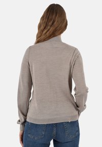 Maglione lavorato a maglia color beige chiaro con maniche lunghe, polsini a coste e dettagli di cucitura sul retro. Il materiale sembra morbido e leggermente texturizzato.