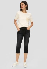 Lichtbeige T-shirt met korte mouwen en een textuur zakje, gecombineerd met zwarte cropped jeans en witte sneakers. Eenvoudige, casual outfit.