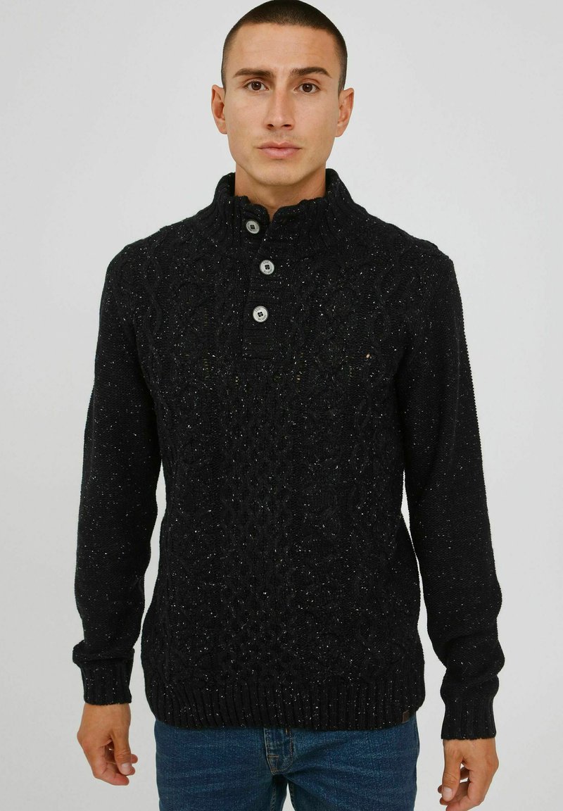 Schwarzer gestrickter Pullover mit hohem Kragen, der ein strukturiertes Muster und drei Knöpfe aufweist. Hergestellt aus einem strukturisierten Stoff mit Flocken.