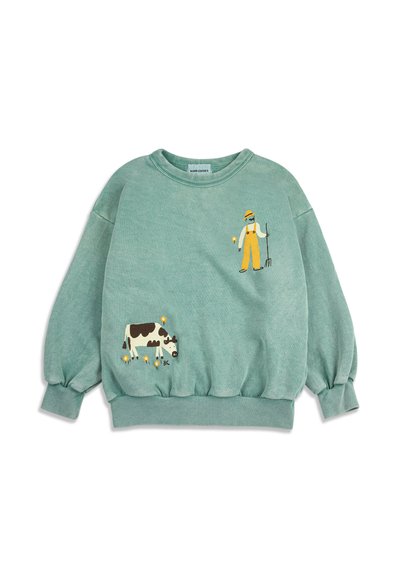 Sweatshirt vert avec des illustrations d'un fermier tenant une fourche et d'une vache noire et blanche en train de paître, accompagnée de petites fleurs jaunes.