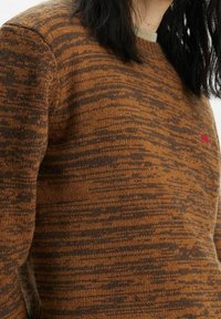 Maglione lavorato a maglia marrone con un motivo a strisce testurizzato in tonalità più scure e un piccolo logo rosso sul petto. Design classico a scollatura rotonda.