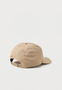 Šviesiai rudos spalvos beisbolo kepuraitė su išlenktu skydeliu, pagaminta iš lengvos medžiagos. Yra snapback užsegimas ir ventiliacijos anga viršuje.