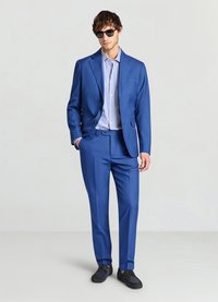 Blauer Anzug mit strukturiertem Blazer und maßgeschneiderten Hosen, getragen über einem gestreiften Hemd; kombiniert mit schwarzen Schuhen und Sonnenbrille.