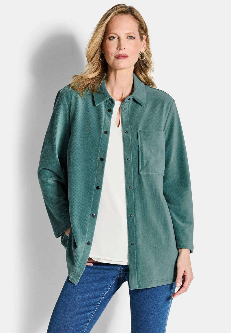 Türkisfarbene Cordjacke mit Knopfverschluss, Kragen und einer Brusttasche. Über einem weißen Oberteil und blauen Jeans gestylt.