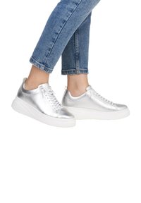 Metallisch silberne Sneaker mit einer glatten, lederähnlichen Textur, Schnürverschluss und einer dicken weißen Sohle. Getragen mit hochgekrempelten Jeans.