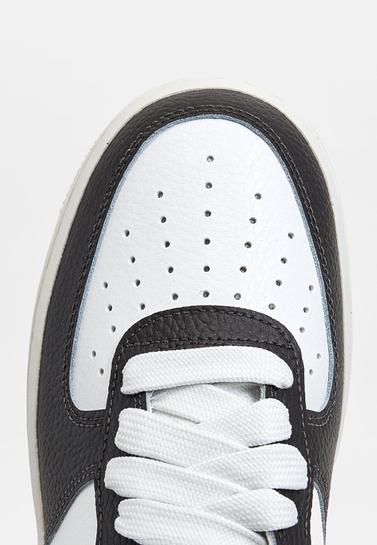 Schwarz-weiße Sneaker mit einem strukturierten Leder-Obermaterial, runder Zehenpartie, durchbrochenen Details und weißen Schnürsenkeln. Haben einen gepolsterten Schaft und Zunge.