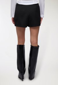 Pantaloncini neri su misura con una texture liscia, caratterizzati da un'orlo dritto. Abbinati a stivali neri lucidi alti fino alla coscia.