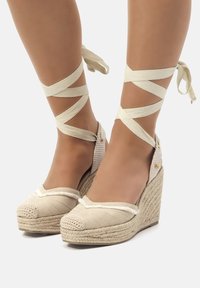 Wedge espadrillas beige con suole in juta intrecciata, materiale superiore testurizzato e cinturini a nastro incrociati che avvolgono le caviglie.