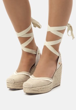 Wedge espadrillas beige con suole in juta intrecciata, materiale superiore testurizzato e cinturini a nastro incrociati che avvolgono le caviglie.