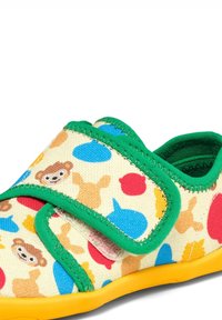 Chaussure pour enfant avec bordure verte et semelle jaune, décorée de formes d’animaux colorées comprenant des ours, des chiens et des poissons sur tissu crème.