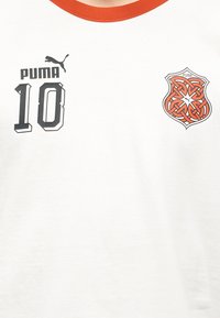 Λευκό πουκάμισο με πορτοκαλί γιακά που φέρει μαύρο λογότυπο "Puma", τον αριθμό 10 και μια περίτεχνη πορτοκαλί και μαύρη ασπίδα στο στήθος.