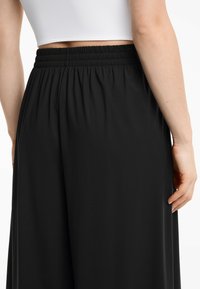 Schwarze weit geschnittene Hosen verfügen über einen strukturierten, elastischen Bund. Das Material wirkt weich und fließend, mit einem eleganten, minimalistischen Design.