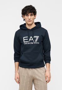 Tengerészkék kapucnis pulóver elől kenguruzsebbel, fehér "EA7 Emporio Armani" logóval. Puha pamutkeverék anyagból készült.
