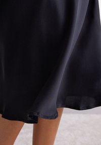 Falda de satén negro con una textura suave, silueta fluida y un dobladillo curvado, que cuenta con una caída ligera y suave.