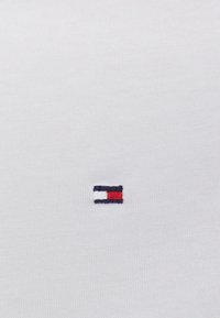 Vit bomullsskjorta med en liten broderad logotyp i marinblått, rött och vitt på vänster bröst. Slät yta med klassisk passform.