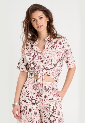 T-shirt à manches courtes, cropped, avec un devant noué, ornée d'un soleil rose et marron ainsi que d'un motif abstrait sur un fond clair.