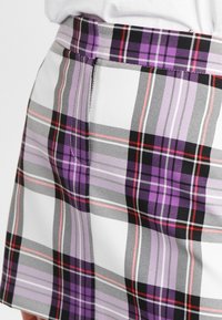 Randig kjol med en blandning av lila, svart och vit färg med röda accenter. Slät tygkvalitet med en figursydd midja och sidoseamsdetaljer.