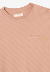 Svietlo ružové rebrované pletené tričko s okrúhlym výstrihom a malou náprsné vreckom s vyšívaným žltým logom "Blkvis".