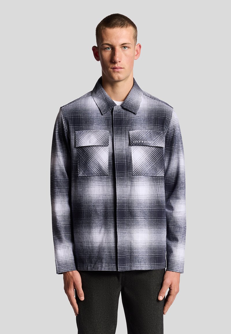 Giacca a quadri in bianco e nero con due tasche sul petto, design con colletto e maniche lunghe, caratterizzata da un tessuto testurizzato e un motivo geometrico.