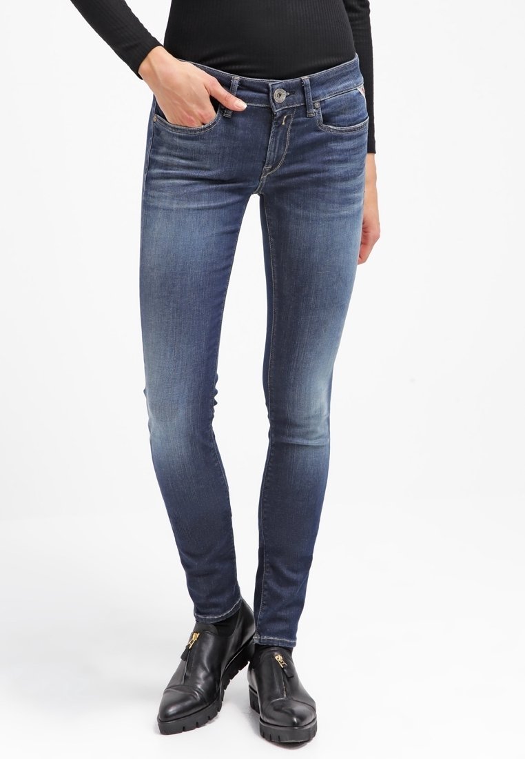 Jeans ajustados en denim azul oscuro, con una cintura de altura media, cinco bolsillos y un ligero desgaste en los muslos. Combinados con botas negras hasta el tobillo.