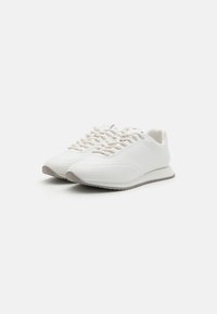 Hvite sneakers laget av glatt materiale med rund tå, har flate lisser, minimalistisk design og en subtil gummisåle.