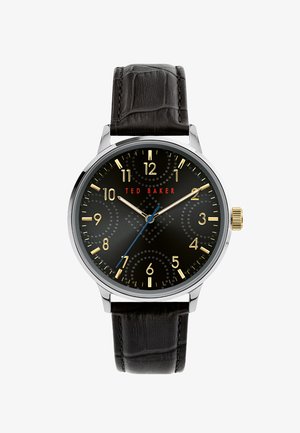 Čierne hodinky značky Ted Baker s pozlátenými indexmi hodín, zlatými a modrými ručičkami, strieborným puzdrom a čiernym koženým remienkom s textúrou.