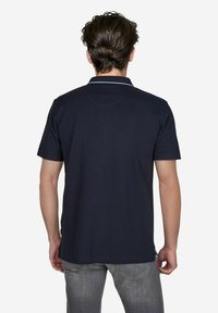 Marineblauwe polo met korte mouwen, klassieke kraag en witte accentstiksels. De stof lijkt glad met een stevige textuur. Minimale branding.