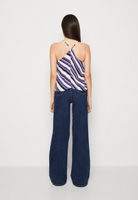 Top senza maniche a righe viola e bianche con spalline incrociate sul retro, abbinato a jeans a gamba larga in denim scuro. Tessuto morbido, vestibilità rilassata.