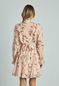 Abito floreale in morbido tessuto rosa con maniche lunghe, dettagli arricciati, uno scollo legato dietro, e gonna a strati con foglie verdi e fiori rosa.