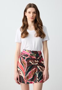 Weißes T-Shirt mit kurzen Ärmeln, kombiniert mit einem mehrfarbigen, gemusterten A-Linien-Rock, der dunkelbraune, rosa und grüne Blättermotive aufweist.