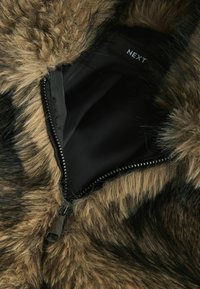 Brown faux fur collar with black accents, featuring a visible zipper and a black lining labeled "NEXT." Soft texture and distinct pattern.