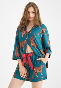 Conjunto de pijama turquesa con estampado de tigre naranja, que incluye una parte superior abotonada y pantalones cortos a juego con lazo rojo. Tejido suave y ajuste relajado.