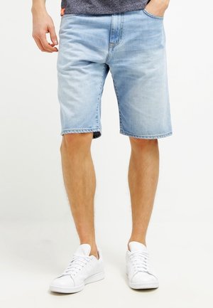 Jasnoniebieskie szorty dżinsowe o luźnym kroju, z pięcioma kieszeniami i surowym wykończeniem na dole. Połączone z białymi sneakersami.