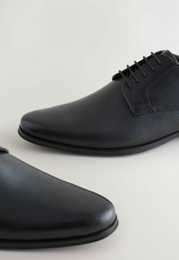 Sorte læder dress sko med en struktureret overflade og spidse tå. Funktioner inkluderer snørebånd og en glat sideakcent.
