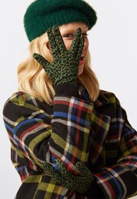 Guanti con stampa a leopardo verde e finitura testurizzata, abbinati a un cappotto a quadri nei colori nero, rosso, blu e verde.