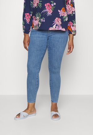 Floral-patterned navy blouse, long sleeves, paired with light blue skinny jeans and light blue slip-on sandals featuring a twist design.