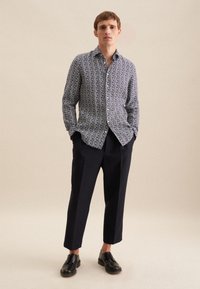 Camicia blu navy con un motivo geometrico bianco, design con bottoni, maniche lunghe, abbinata a pantaloni neri a 3/4 e scarpe nere.