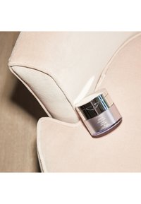 Glasbehälter mit einem silbernen Deckel, der Creme enthält. Das Glas befindet sich am Rand eines weichen, abgerundeten, hellrosa Samtsessels.