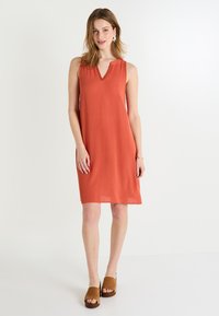 Vestido sin mangas de color óxido con escote en V, tejido texturizado y forma en A. Combinado con mule de punta abierta en color marrón. Diseño simple y casual.
