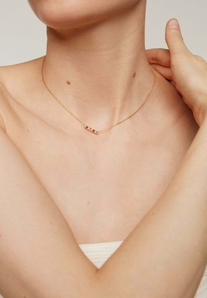 Collar de color dorado con cadena delicada que presenta una barra horizontal adornada con pequeñas piedras preciosas. Diseño sencillo, estética minimalista.