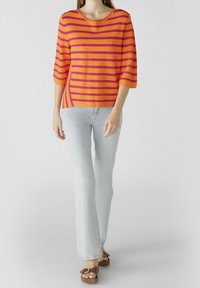 Haut en tricot rayé orange et rose avec des manches trois-quarts, associé à un jean bleu clair et des sandales à talons carrés marron.