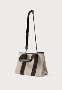 Plátěná taška v béžové barvě s tmavohnědými pruhy, s černým zipem a nastavitelným ramenním popruhem pro všestranné možnosti nošení.