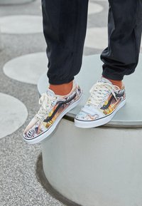 Sneaker multicolori con stampa grafica e suole in gomma bianca. I lacci sono beige; le scarpe hanno un design low-top con motivi misti.