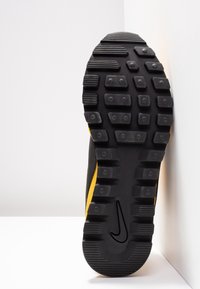 Svart sneakersula med framträdande gula detaljer, texturerat gummi för grepp, med ett distinkt mönster och en swoosh-logotyp.