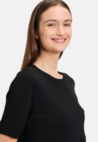Top corto a maniche corte in maglia nera, con scollatura tonda, texture liscia e silhouette aderente, che si adagia delicatamente sulle spalle.