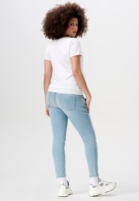 Lichtblauwe skinny jeans met achterzakken, gedragen met een witte t-shirt met korte mouwen en witte sneakers met grijze accenten.