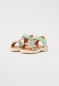 Vihreät ja vaaleanpunaiset lasten sandaalit, joissa on kiiltävä, teksturoitu glitter-nauha, tarrakiinnitys ja pehmustettu beige pohja.