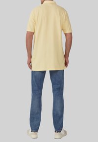 Żółta koszulka polo z krótkimi rękawami, noszona na niebieskich dżinsach. Posiada klasyczny kołnierzyk i boczne rozporki. Białe trampki dopełniają strój.
